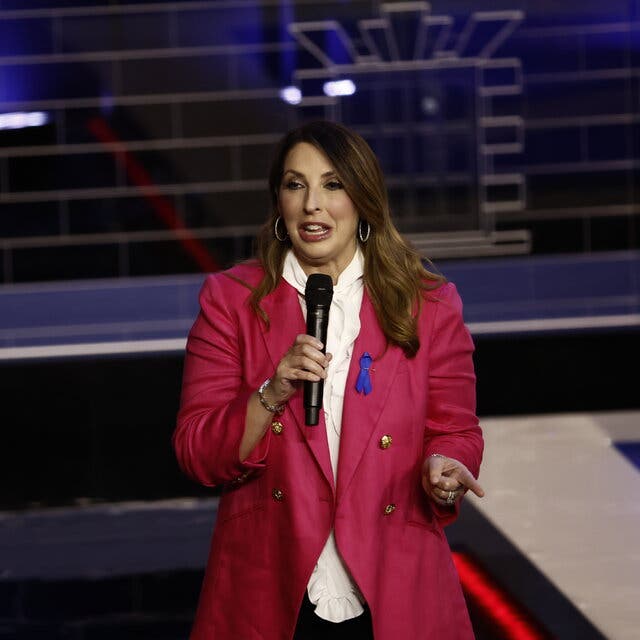 Ronna McDaniel, wearing a red jacket and holding a microphone, gestures as she speaks.
