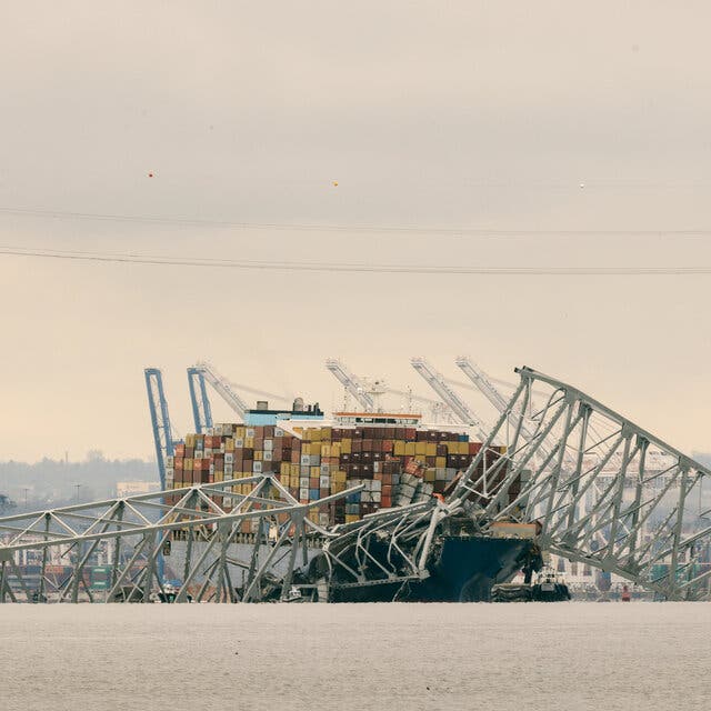 A twisted metal section of the bridge is draped over the cargo ship.