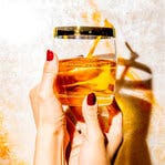 Manicured hands hold an amber-colored drink.