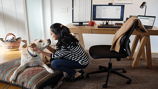 Femme travaillant à distance depuis son bureau à domicile, prenant une pause et caressant son chien ; appareil Dell Latitude 13.
